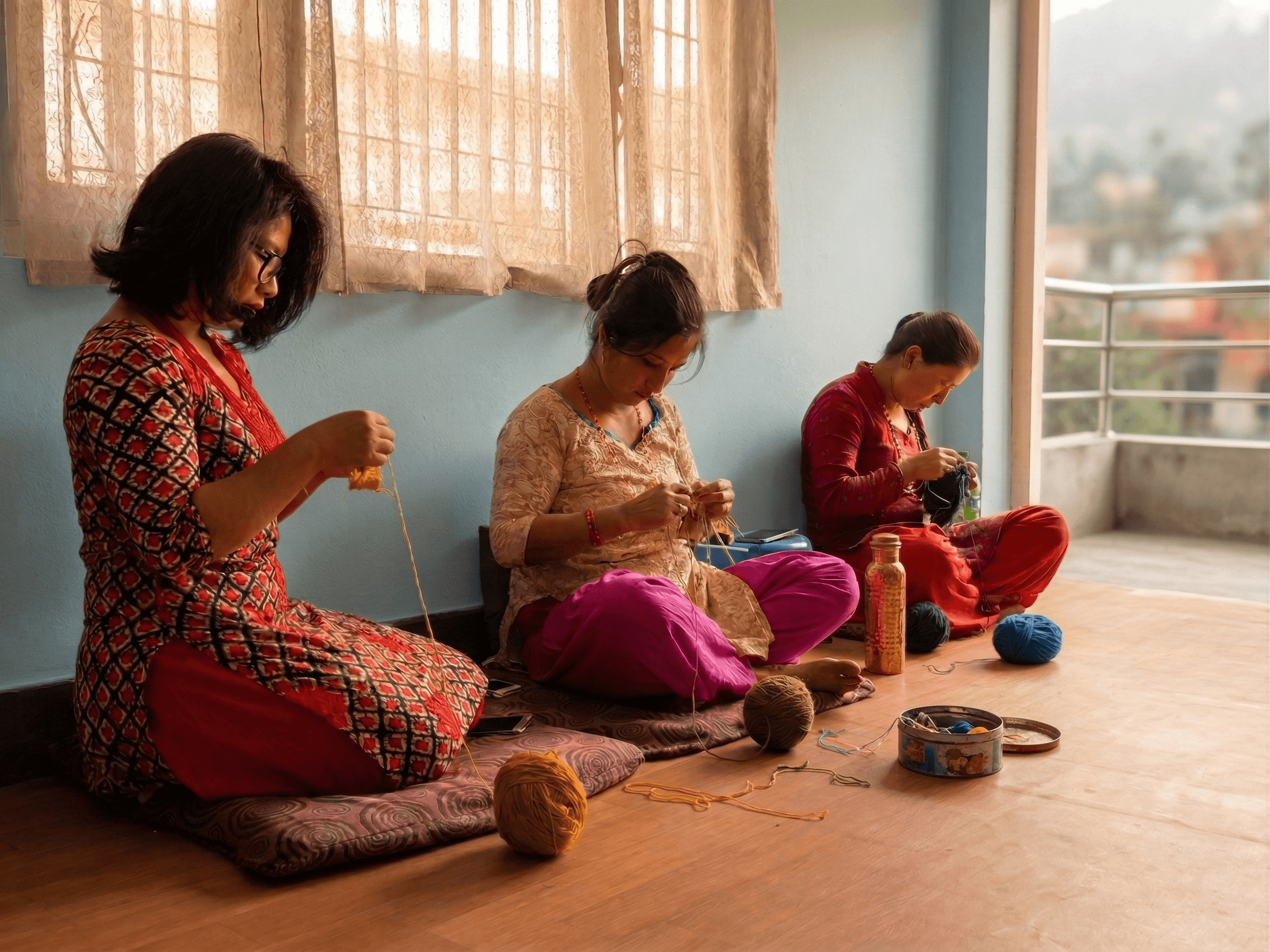 Group of women sitting together knitting colorful wool garments in a courtyard